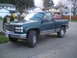 1985 Ford Bronco II - A green GMC pickup truck is parked on a paved surface in front of houses.