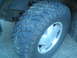 1985 Ford Bronco II - A close-up view of a vehicle's tire and wheel assembly, showing off-road tread and a silver rim.