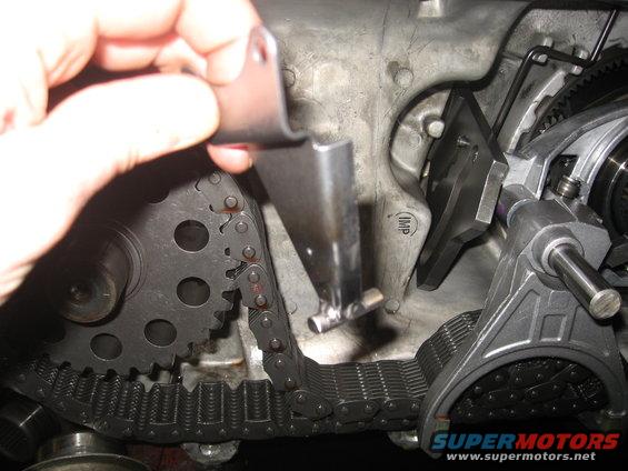 Hand holding metal bracket over engine timing chain and gears