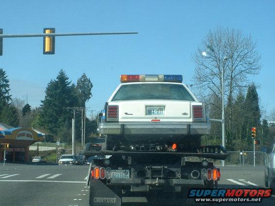 1987 Ford Crown Victoria LTD police car on a tow truck, rear view. License plate 98J-VJT