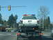 1987 Ford Crown Victoria LTD - Police car being towed on a flatbed truck, seen from behind at an intersection.