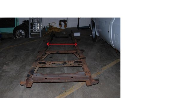 Vehicle frame on concrete floor with red arrows indicating a measurement