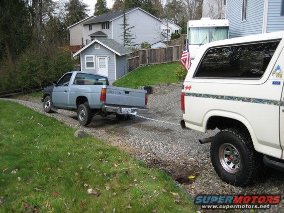 Nissan pickup truck chained to a white Ford Bronco in a driveway
