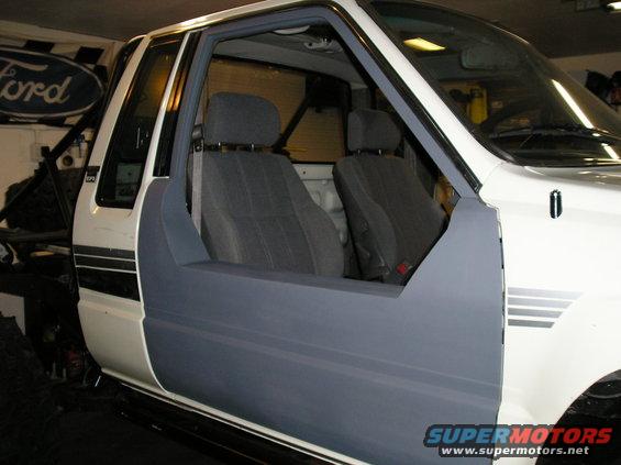 1986 Toyota Hilux interior showing grey seats and primer grey door panel. Roll cage visible behind seats