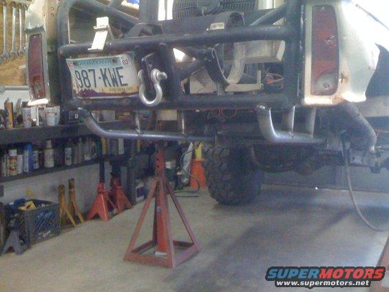 Rear of a modified off-road vehicle on jack stands, showing a roll cage and a license plate