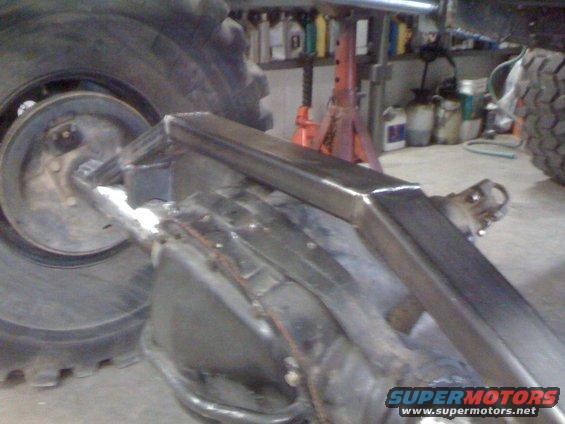Close-up of a custom suspension component welded onto a vehicle's rear axle, with a large tire visible