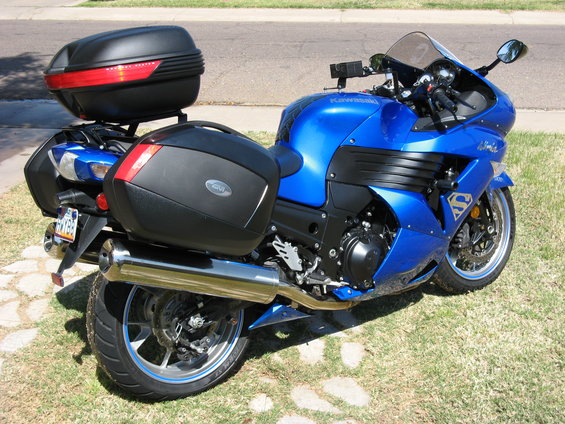 Blue Kawasaki motorcycle with Givi saddlebags and a black top case, parked on grass