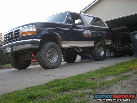 Dark blue Ford Bronco with lifted suspension and large tires parked in a driveway