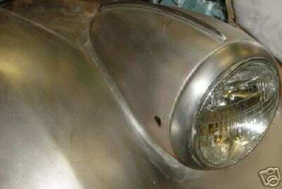Close-up of a car's front fender and headlight assembly, showing unpainted metal