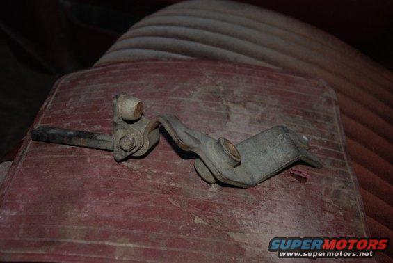 Transfer case shifter linkage part on a red surface, with ribbed upholstery in the background