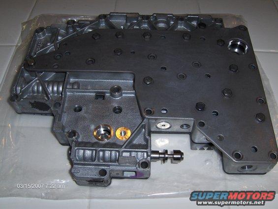 Metal valve body with various bolts and ports, some brass fittings visible