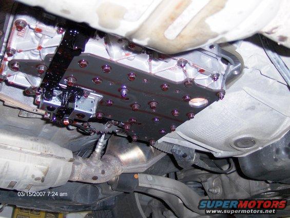 underside of a car showing the transmission valve body with purple bolts and some fluid drips