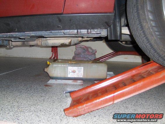 Red car's undercarriage with exhaust pipe and oil drain pan on the ground