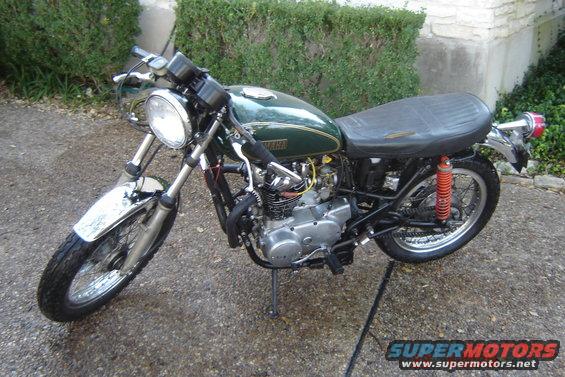 Green motorcycle parked on a driveway. It has a black seat and chrome fenders