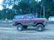 1979 Ford Bronco - A muddy maroon Ford Bronco is seen from the side during an off-road event.