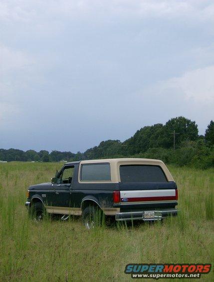 Dark blue and tan 1990 Ford Bronco parked in tall grass, rear quarter view