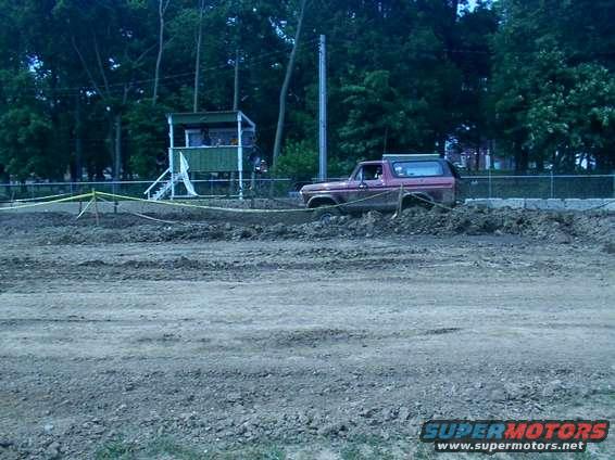 Red 1978 Ford Bronco stuck in a muddy track with a green observation booth in the background