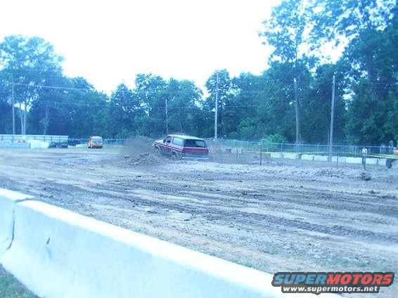 Red SUV kicking up dirt on a muddy track, viewed from the side