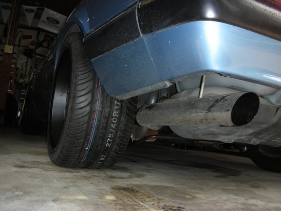 Blue car's wide rear tire and exhaust pipe, seen from low angle