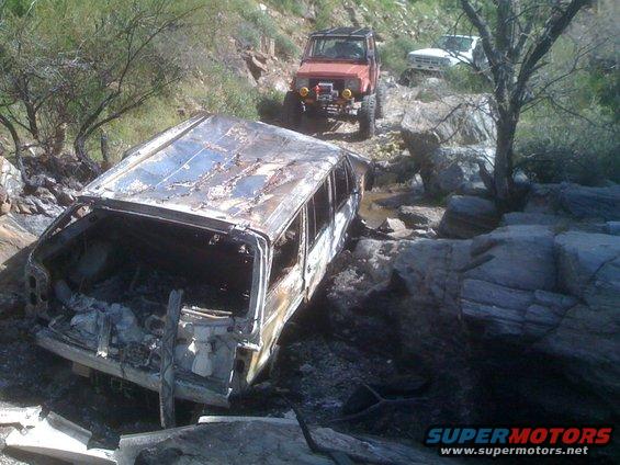 Burnt-out SUV on rocky trail with two other off-road vehicles behind it