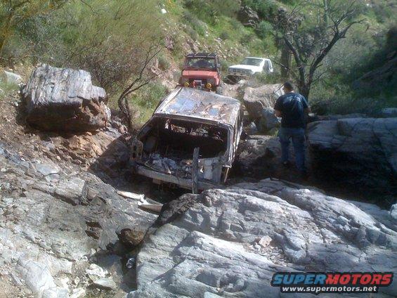 Wrecked vehicle in rocky terrain with two other off-road vehicles behind it