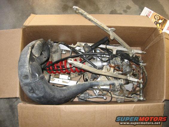 Motorcycle engine and exhaust pipe in a cardboard box. Some parts are disassembled
