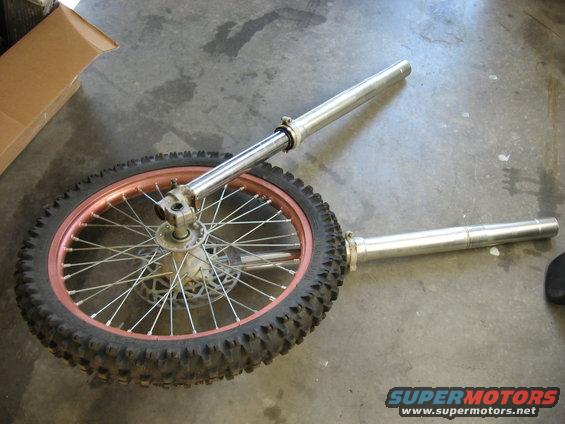 Motorcycle front wheel with copper rim and suspension forks on a concrete floor