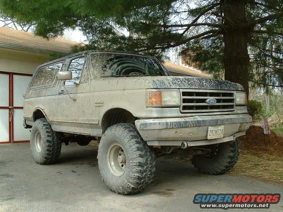 Mud-covered 1991 Ford Bronco with large off-road tires parked outside a garage