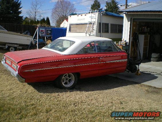 red two-door hardtop car with white roof, parked on grass next to a garage and RV