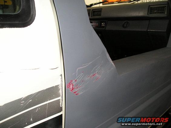 Gray truck side panel with red and white scratches, showing part of the interior dashboard and door