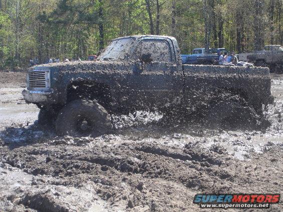 Mud-covered pickup truck stuck in mud, with other vehicles in background