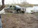 1996 Ford Bronco - Green crew cab pickup truck stuck in mud near a body of water.