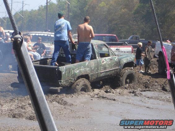Green pickup truck stuck in mud with people in the bed