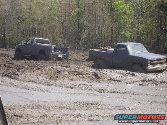 Dark blue pickup truck stuck in mud, front right wheel submerged