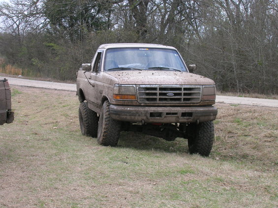 Mud-covered pickup truck with lifted suspension and large tires, front view