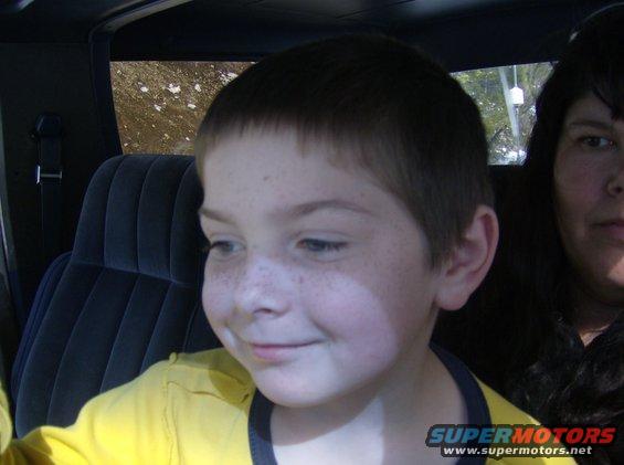 Interior view of a vehicle with a young boy in the foreground and a woman behind him