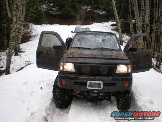 Black off-road truck with open doors in snow, another vehicle behind