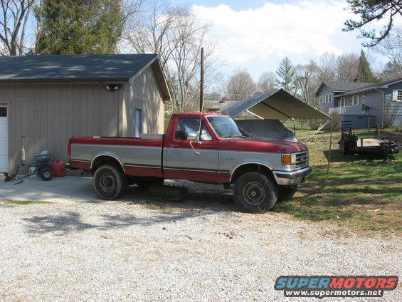 1987 Ford F-150 pickup truck, red and silver two-tone paint, parked on gravel in front of a garage