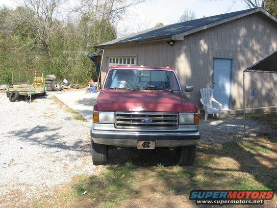 Red Ford pickup truck parked in front of a garage. License plate is visible