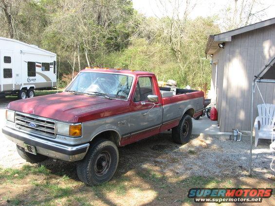 Two-tone red and gray Ford F-250 pickup truck with a cracked windshield parked on gravel