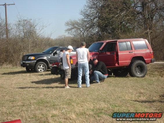 Red SUV with open door and people working on tire. Another dark SUV parked nearby