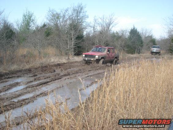 Red Jeep Cherokee XJ driving through mud, another SUV behind it