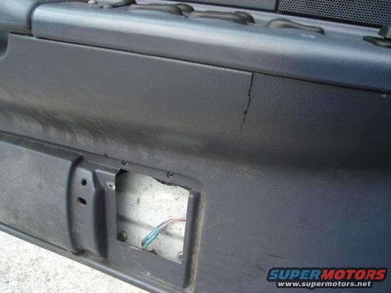 Close-up of a dark gray interior door panel with a visible crack and an open section revealing wires
