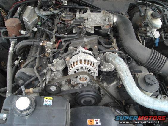 Engine bay with alternator, belts, and hoses visible. Some corrosion on metal parts
