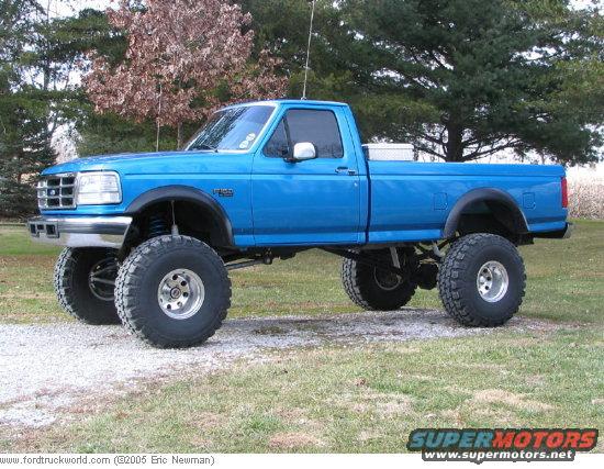 Blue lifted pickup truck with large tires parked on gravel