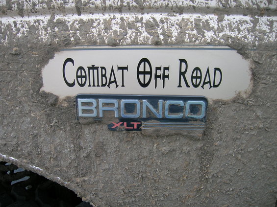 Mud-covered Ford Bronco XLT badge and 'Combat Off Road' decal on a white surface
