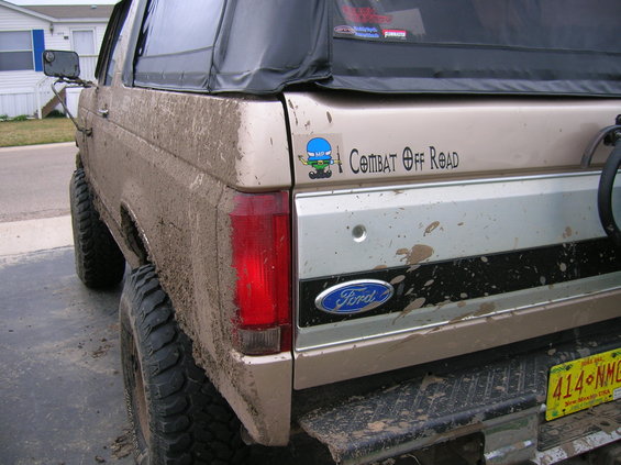 Mud-covered tan SUV rear quarter panel with Ford logo and 'Combat Off Road' sticker