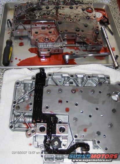 Transmission valve body disassembled on a tray with a screwdriver and ratchet