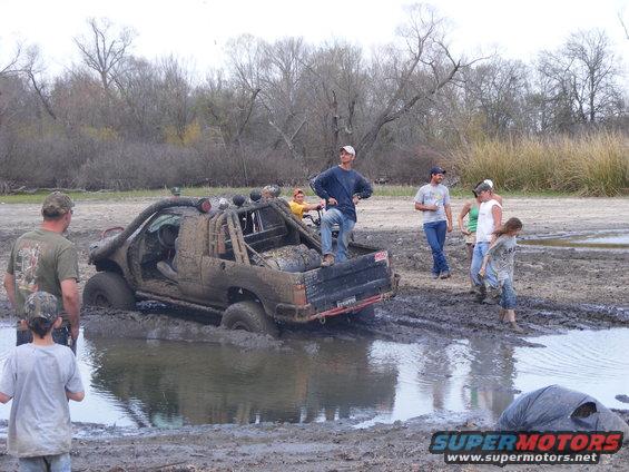 Muddy pickup truck stuck in water hole, people watching
