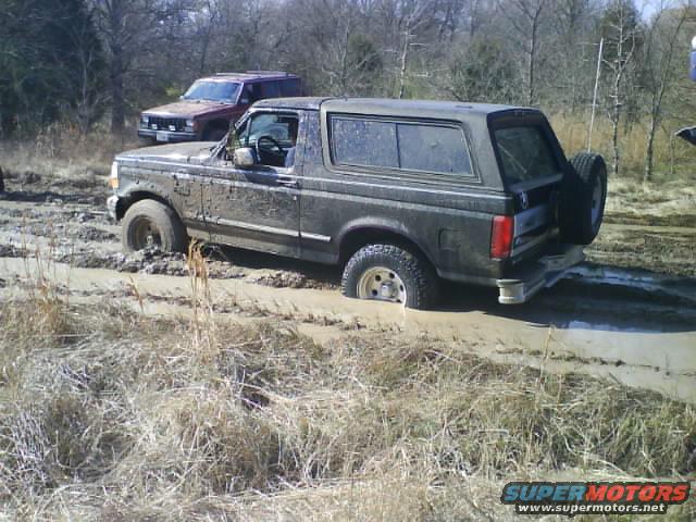Muddy 1992 Ford Bronco stuck in mud, with a red SUV behind it